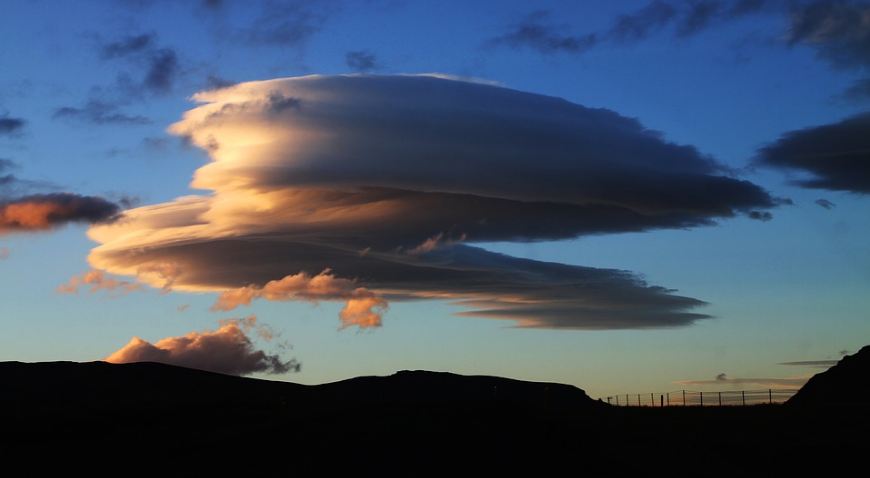 a-silhouette-of-a-hill-and-a-large-circular-clouds