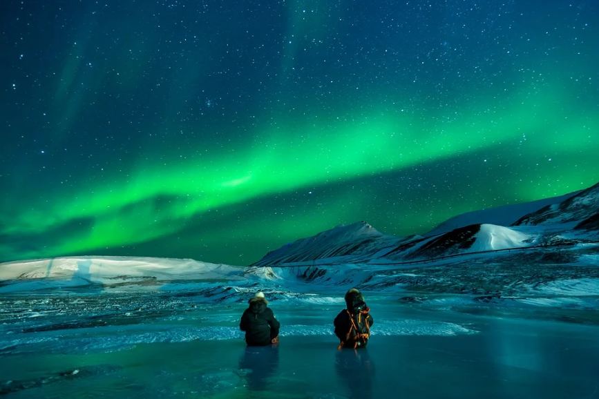 men sitting watching the northern lights in the night sky