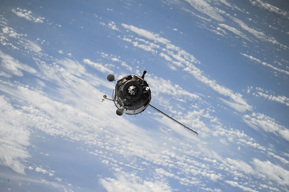 small circular satellite, blue sky with white sheets of clouds