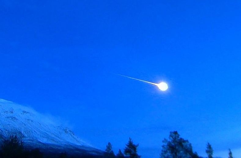 a bright and giant Taurid meteor, meteor heading to the right, blue sky, a mountain, and trees