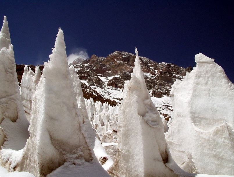 tall and large ice formations, brown mountains partially covered in snow, blue sky